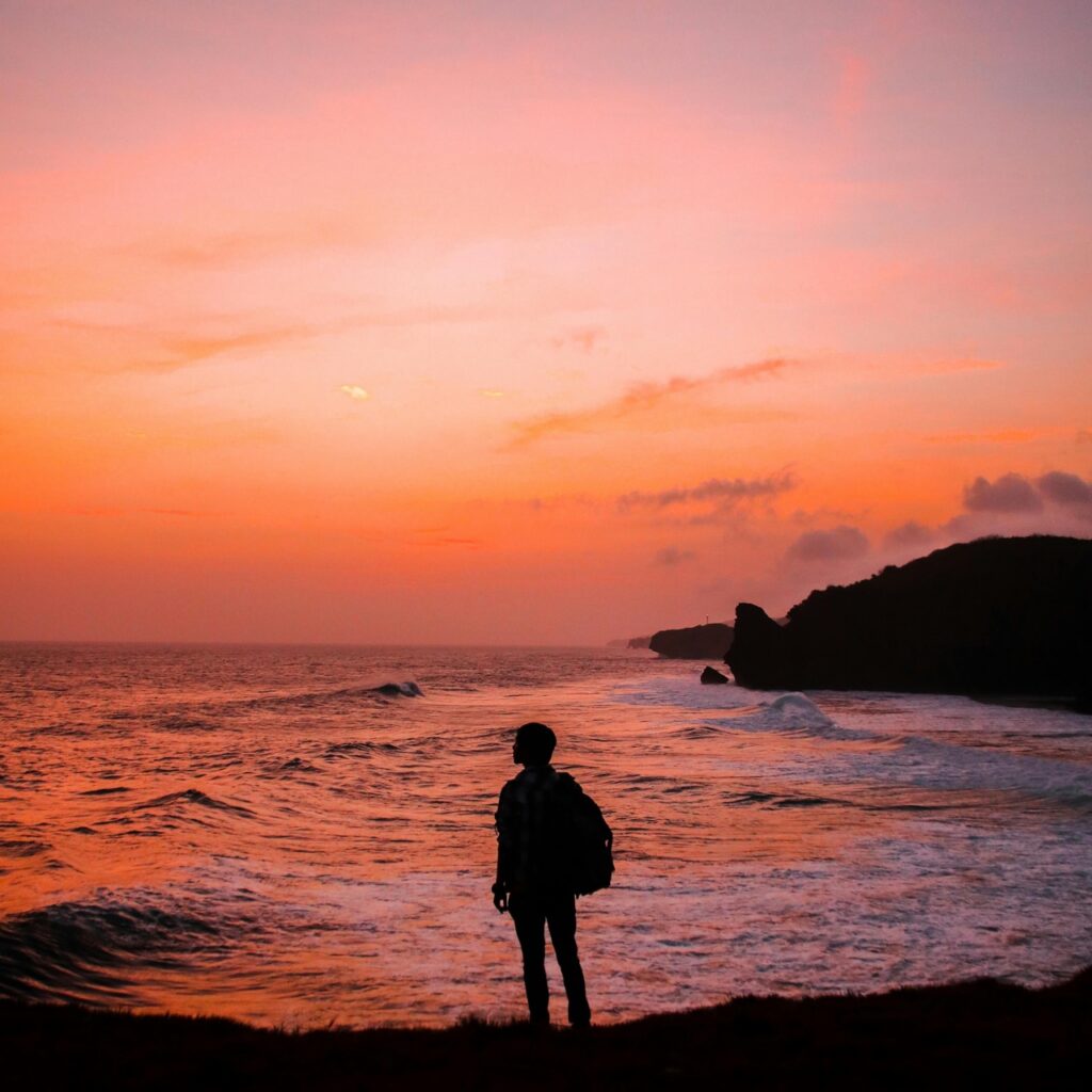 Silhouette d'une personne face à la mer au coucher du soleil